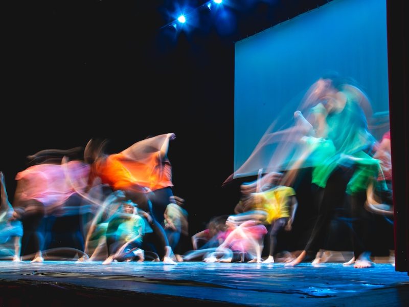 Group of dancer in colored clothes dancing on the stage in long exposure Group of dancer in colored clothes dancing on the stage in long exposure. Dark background